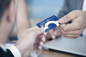 Close-up Of Two Businessmen Holding Card Over Desk